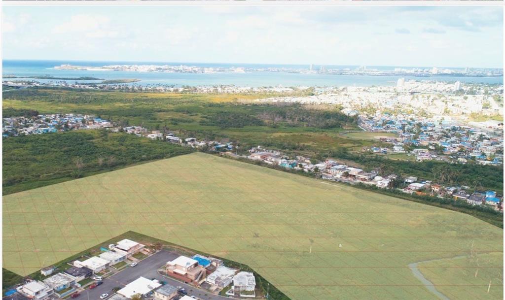 An aerial view shows a large, vacant grassy lot bordered by residential houses and vegetation — 28 ACRES VACANT RESIDENTIAL LAND – CATAÑO, PUERTO, CATANO, PR