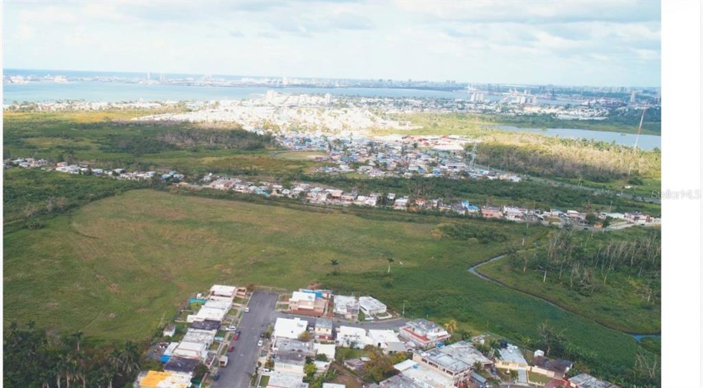 An aerial view shows a residential neighborhood bordering a large, undeveloped grassy field and wetlands — 28 ACRES VACANT RESIDENTIAL LAND – CATAÑO, PUERTO, CATANO, PR