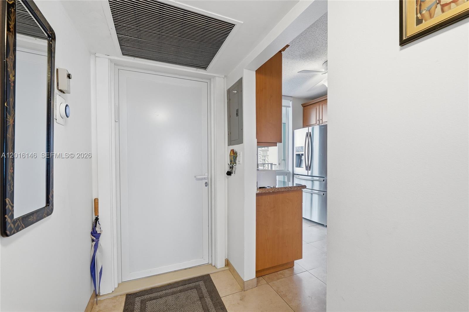 An entryway with a white door, a mirror, and an adjacent kitchen with wooden cabinets — 521 N Riverside Dr # 606, Pompano Beach FL 33062, POMPANO BEACH, FL