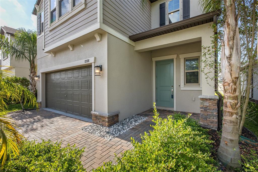 A house exterior features a brown garage door, a teal front door, and stone accents — 8598 CAMPUS WOODS WAY, NEW PORT RICHEY, FL