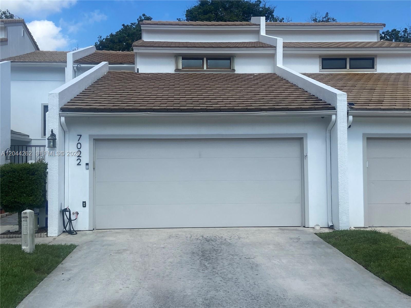 A white townhouse exterior features a two-car garage, a concrete driveway, and brown roof tiles — 7022 Edgemere Ter, Palm Beach Gardens FL 33410, PALM BEACH GARDENS, FL
