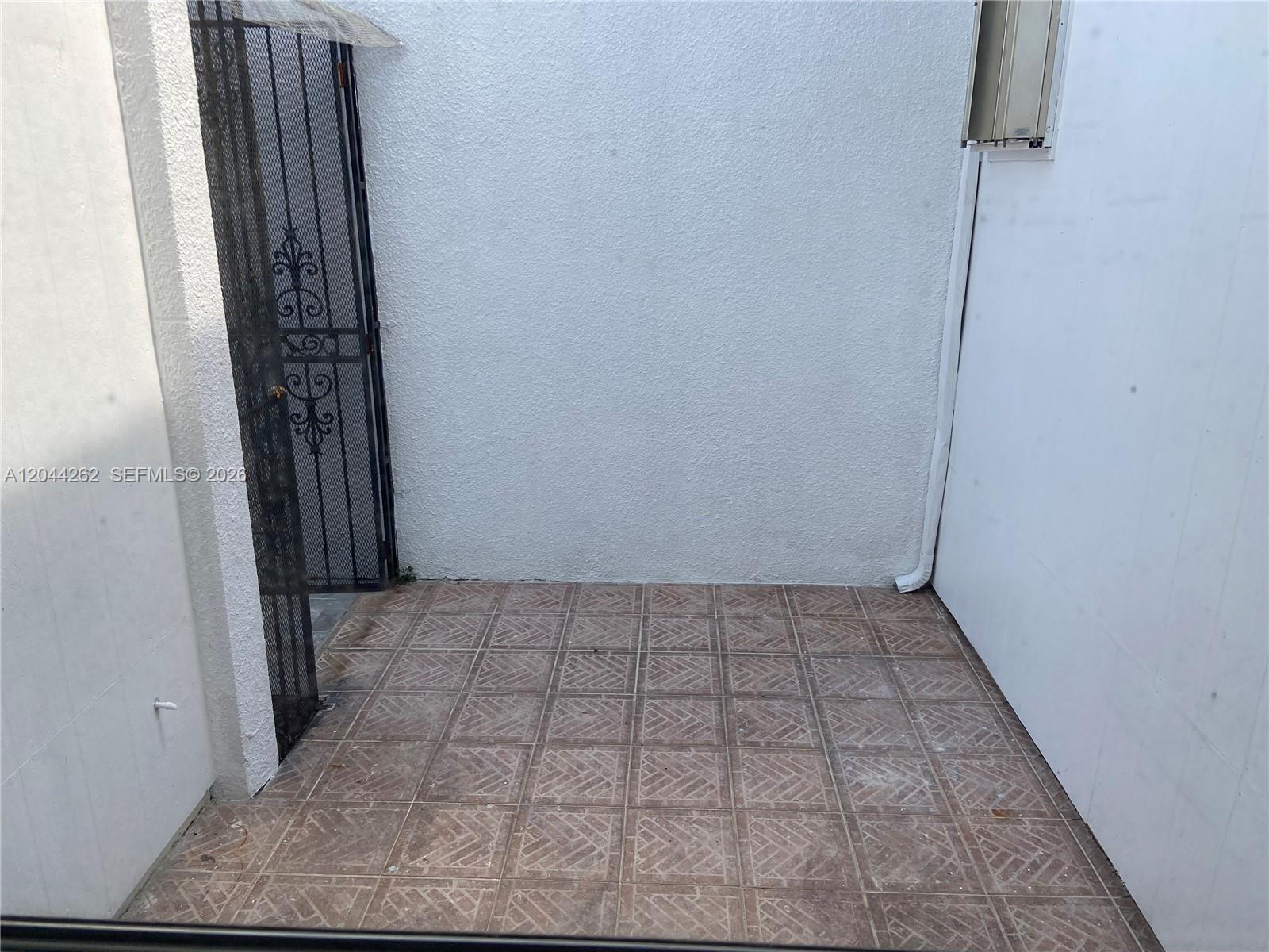 A small, tiled outdoor patio is enclosed by white walls and a black metal gate — 7022 Edgemere Ter, Palm Beach Gardens FL 33410, PALM BEACH GARDENS, FL