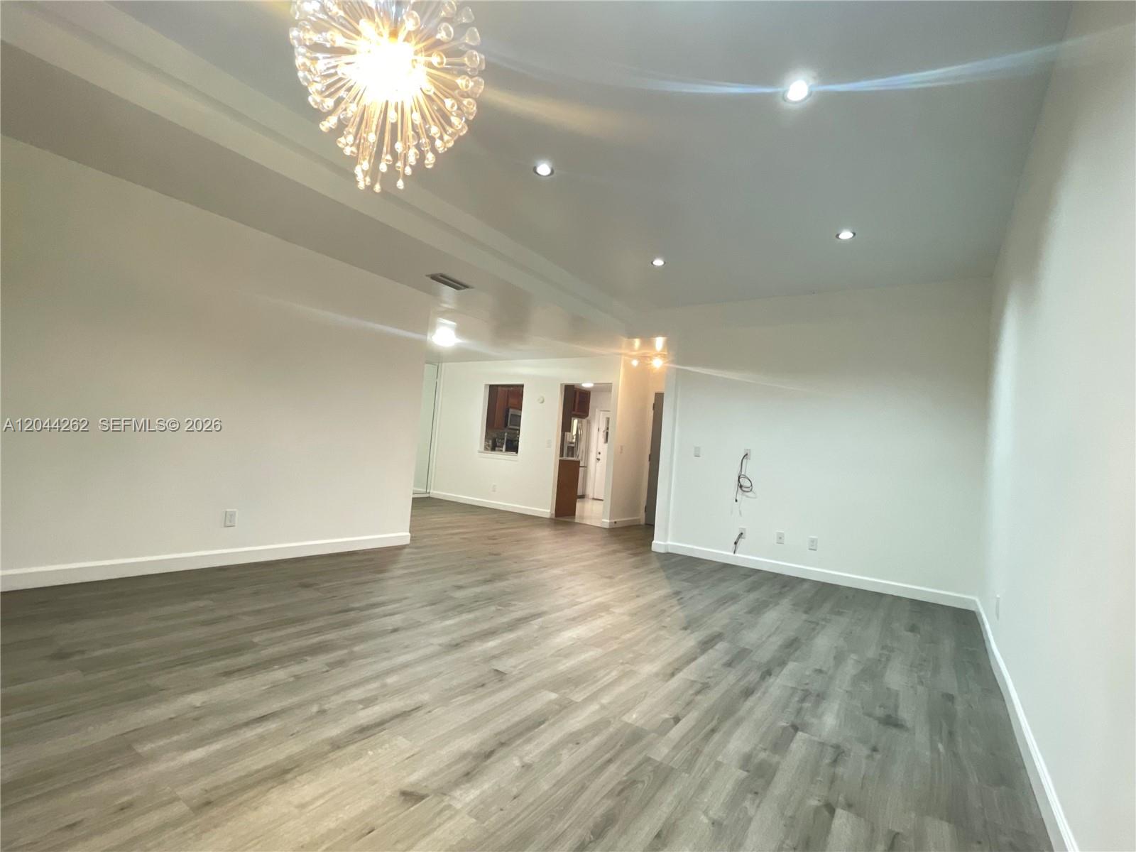An empty room features gray wood-look flooring, white walls, recessed lighting, and a modern chandelier — 7022 Edgemere Ter, Palm Beach Gardens FL 33410, PALM BEACH GARDENS, FL