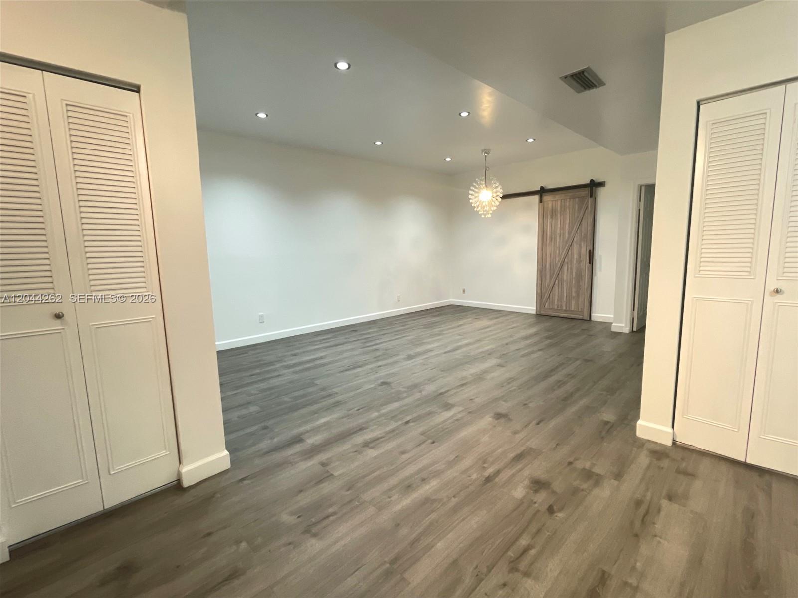 An empty room features white walls, recessed lighting, a barn door, and wood-look flooring — 7022 Edgemere Ter, Palm Beach Gardens FL 33410, PALM BEACH GARDENS, FL