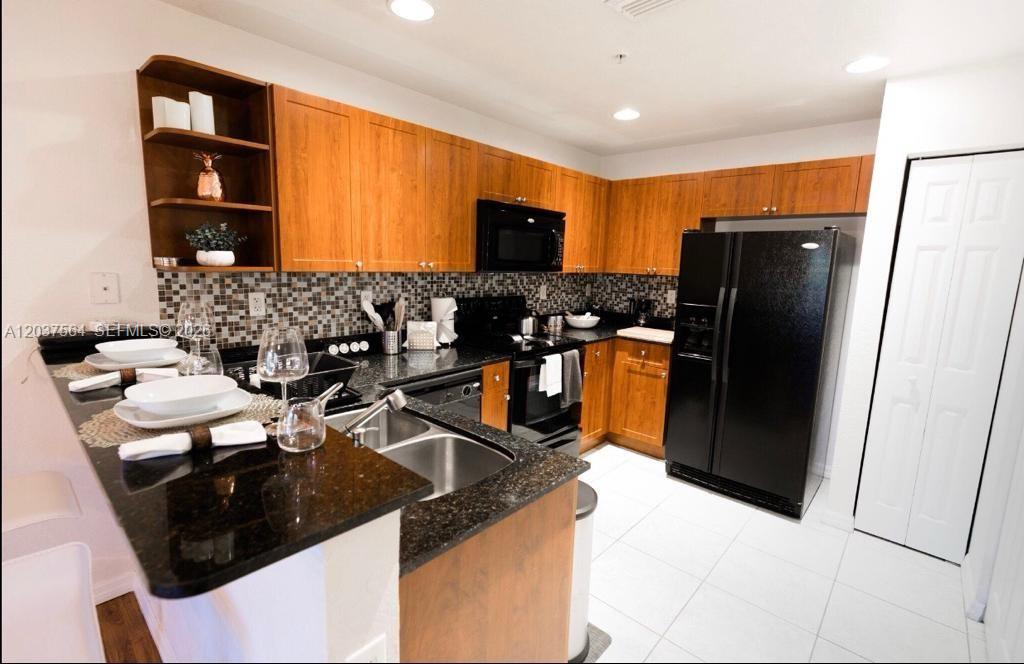A kitchen features wood cabinets, black appliances, dark granite countertops, and a mosaic tile backsplash — 10805 NW 89th Ter # 4, Doral FL 33178, DORAL, FL