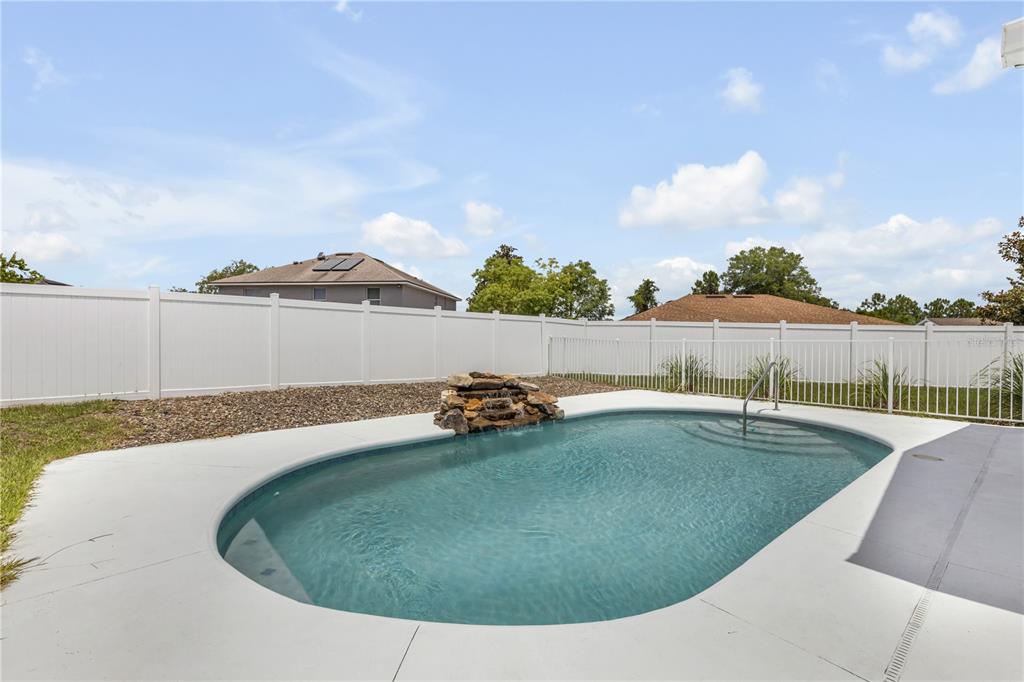 A backyard features a swimming pool with a rock waterfall and a white vinyl fence — 1510 BRAYTON CIRCLE, DELTONA, FL