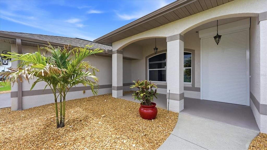 A covered entryway features a concrete walkway, a red potted plant, and a roll-down shutter — 828 ROTONDA CIRCLE, ROTONDA WEST, FL