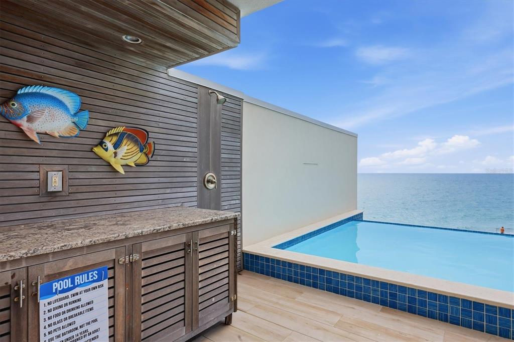 An outdoor pool deck features a shower, wooden cabinetry, fish wall art, and ocean views — 2708 N BEACH ROAD UNIT 3, ENGLEWOOD, FL