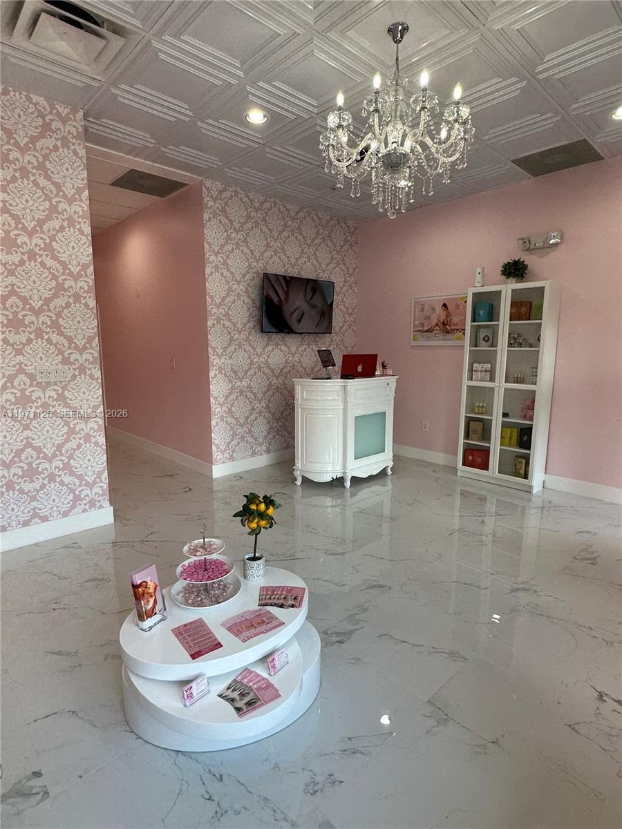 A pink-themed reception area features damask wallpaper, a crystal chandelier, and white marble flooring — CORAL SPRINGS, FL