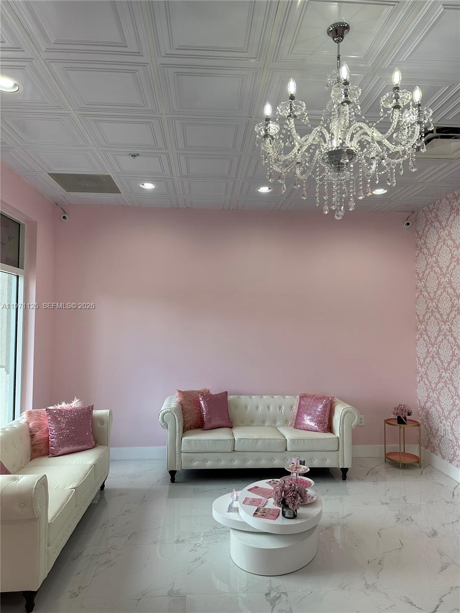 A waiting area features two white tufted sofas, a chandelier, and pink-themed decor — CORAL SPRINGS, FL