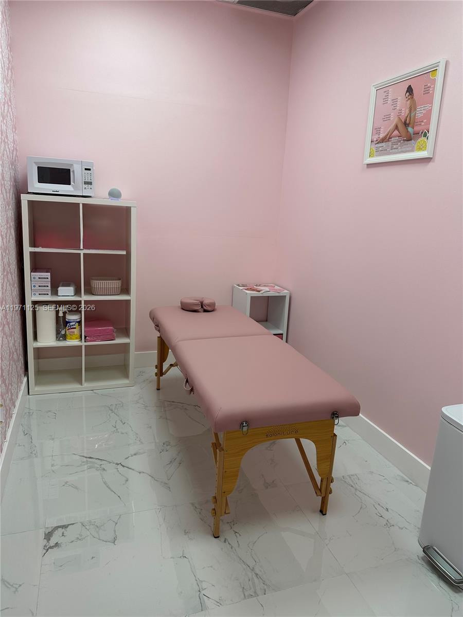 A small treatment room features a pink massage table, white shelving, and marble-patterned flooring — CORAL SPRINGS, FL