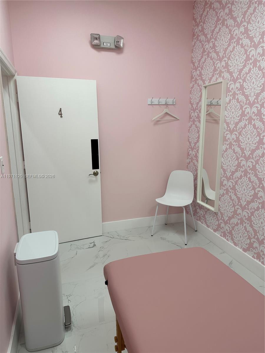 A small room features pink walls, patterned wallpaper, a white door, and a treatment table — CORAL SPRINGS, FL