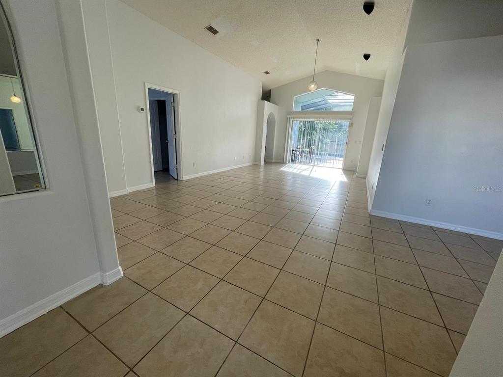 An open-concept living area features light-colored tile flooring, vaulted ceilings, and sliding glass patio doors — 4718 PRAIRIE POINT BOULEVARD, KISSIMMEE, FL