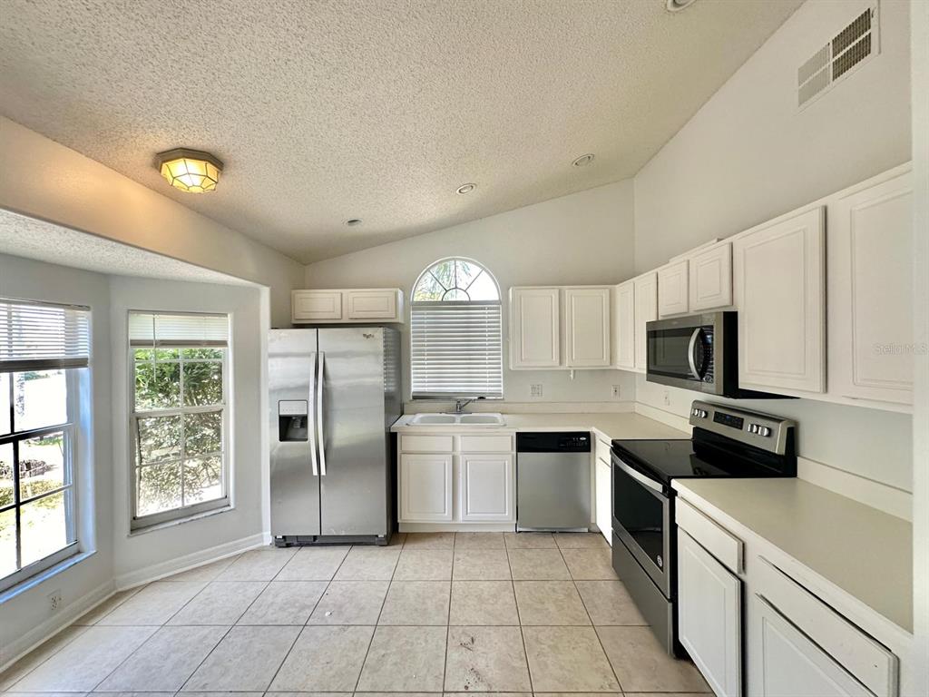 A kitchen features white cabinets, stainless steel appliances, tile flooring, and a vaulted ceiling — 4718 PRAIRIE POINT BOULEVARD, KISSIMMEE, FL