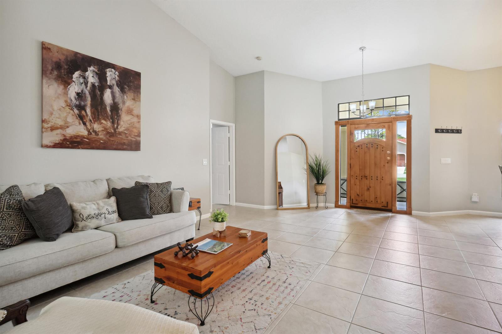 A living room with tile floors, a wooden coffee table, and a front door entrance — 13823 Callington Drive, Wellington FL 33414, WELLINGTON, FL