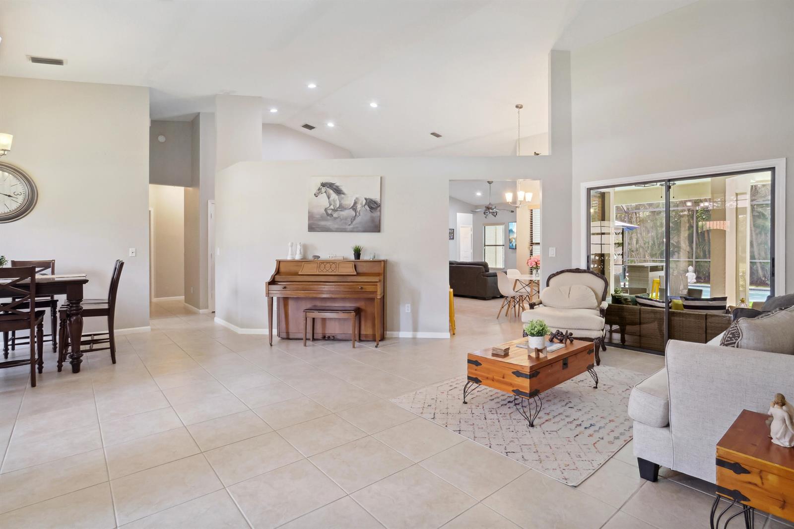 A spacious living and dining area features tile flooring, a piano, and sliding glass doors — 13823 Callington Drive, Wellington FL 33414, WELLINGTON, FL