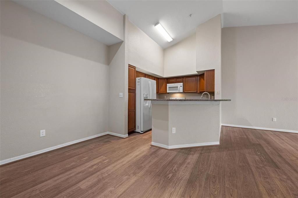 A kitchen with wood cabinets and a breakfast bar opens into a living area — 4174 CENTRAL SARASOTA PARKWAY UNIT # 233, SARASOTA, FL