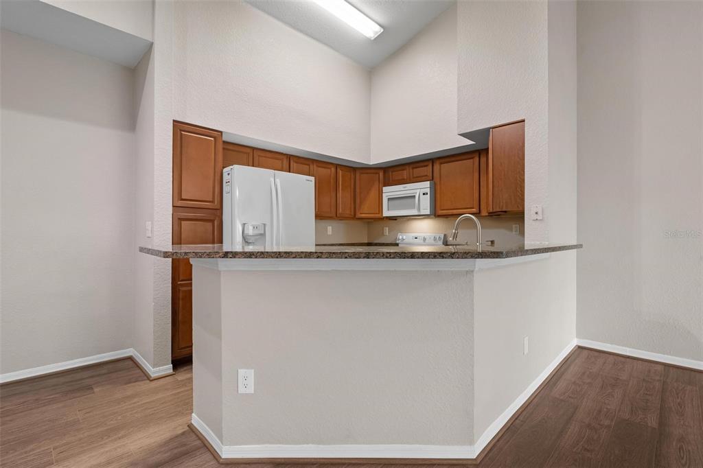 A kitchen features wood cabinets, granite countertops, a white refrigerator, and a breakfast bar — 4174 CENTRAL SARASOTA PARKWAY UNIT # 233, SARASOTA, FL