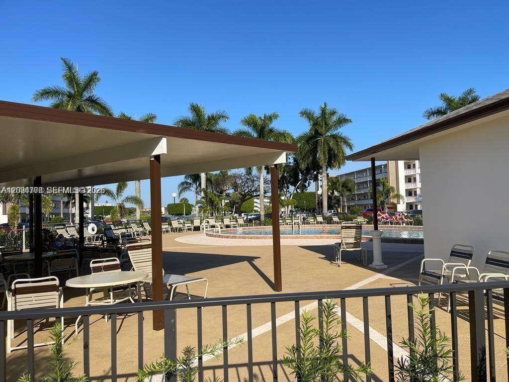 A swimming pool area features a covered patio, lounge chairs, and palm trees under blue skies — 3069 Cornwall D # 3069, Boca Raton FL 33434, BOCA RATON, FL