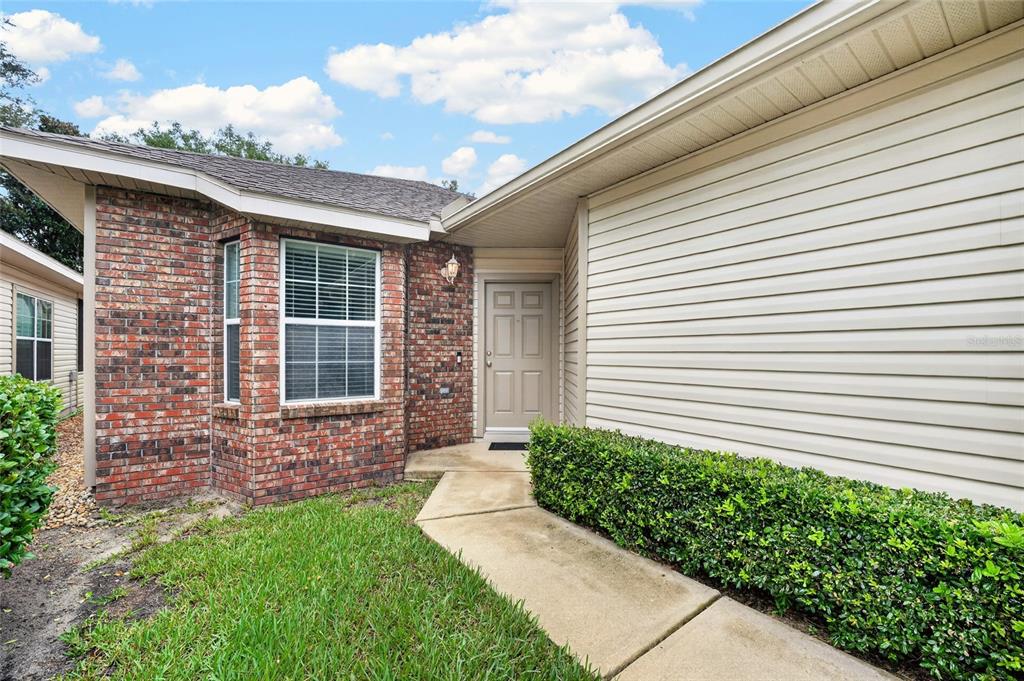 A beige front door is set between a brick-accented wall and light-colored horizontal siding — 7958 NW 49TH WAY, GAINESVILLE, FL