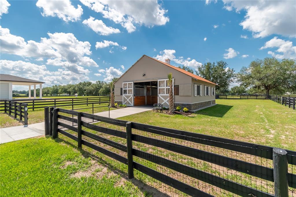 A tan horse barn with white trim stands in a grassy field with black fencing — 6957 NW 54TH LOOP, OCALA, FL