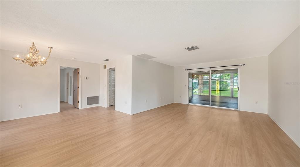 An empty living room features light wood-look flooring, white walls, and sliding glass patio doors — 515 ROUSSEAU DRIVE, NOKOMIS, FL