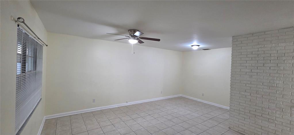 An empty room features light-colored tile flooring, a ceiling fan, and a white brick wall — 6717 MORNAY CIRCLE, TAMPA, FL