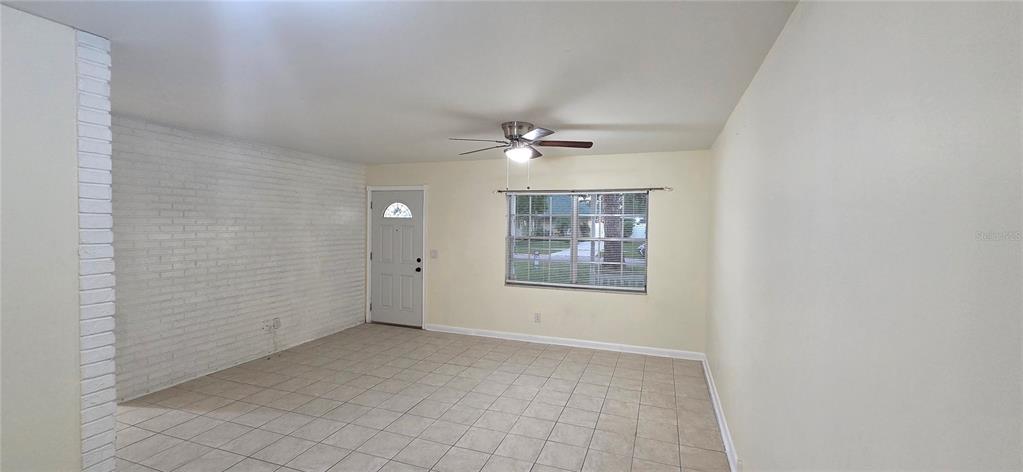 An empty living room features light-colored tile flooring, a white brick wall, and a ceiling fan — 6717 MORNAY CIRCLE, TAMPA, FL