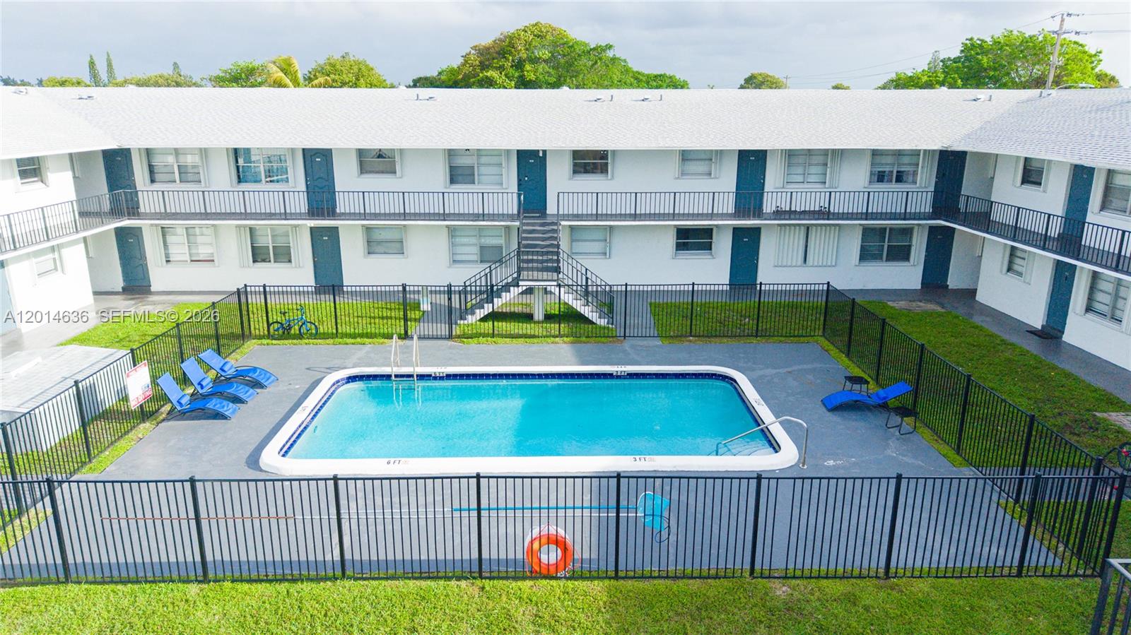 An outdoor swimming pool is enclosed by a black fence in front of an apartment building — 311 NW 42ND CT # 101, Pompano Beach FL 33064, POMPANO BEACH, FL