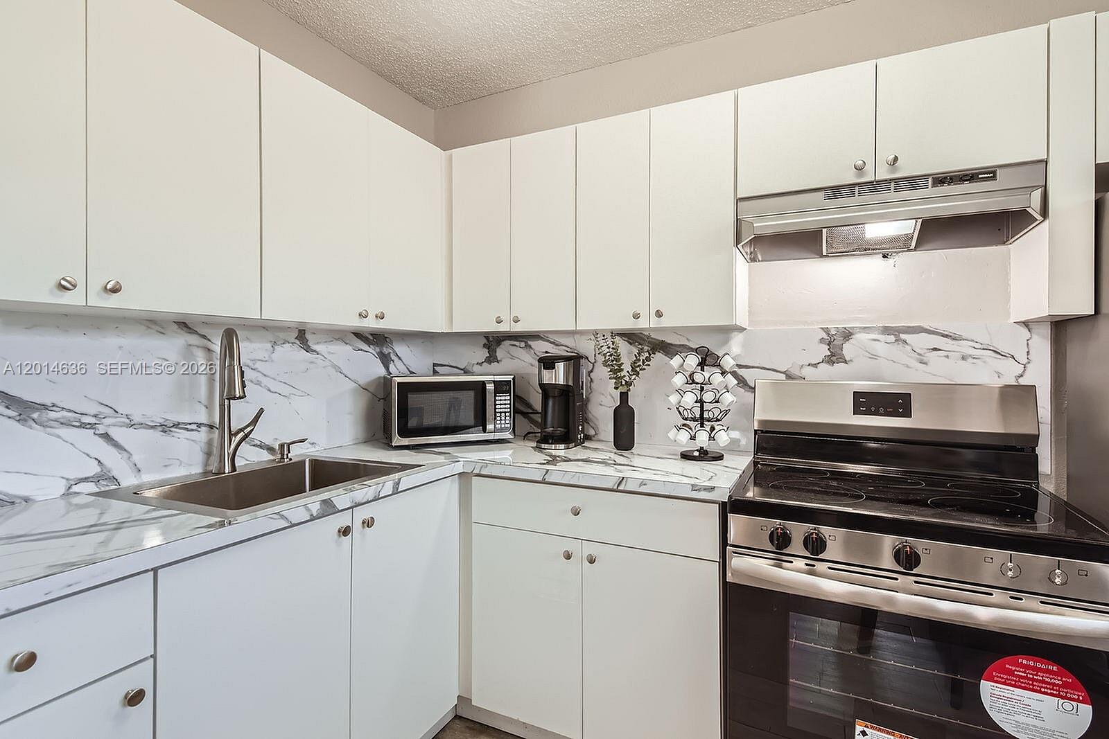A kitchen features white cabinets, marble-patterned countertops, a stainless steel stove, and a sink — 311 NW 42ND CT # 101, Pompano Beach FL 33064, POMPANO BEACH, FL