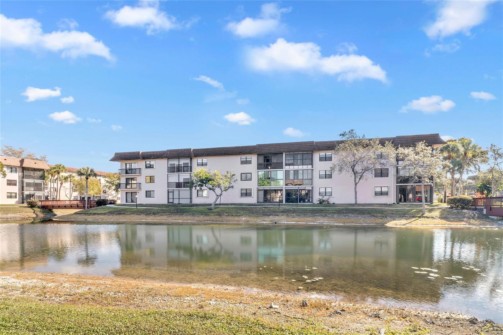 A multi-story apartment building sits behind a pond with a small wooden bridge — 4975 E Sabal Palm Boulevard # 408, Tamarac FL 33319, TAMARAC, FL
