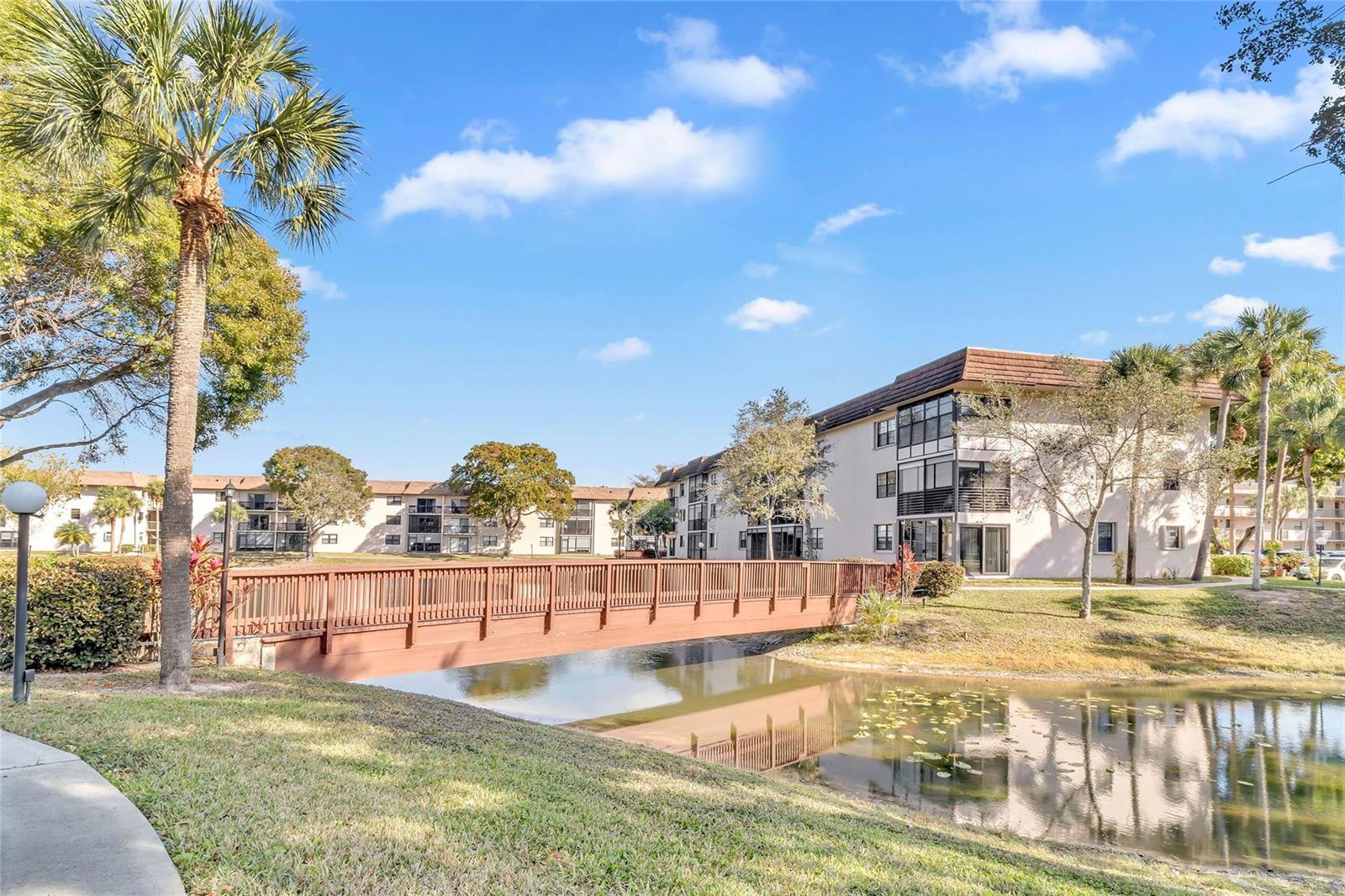 A wooden footbridge crosses a small pond in front of multi-story apartment buildings — 4975 E Sabal Palm Boulevard # 408, Tamarac FL 33319, TAMARAC, FL