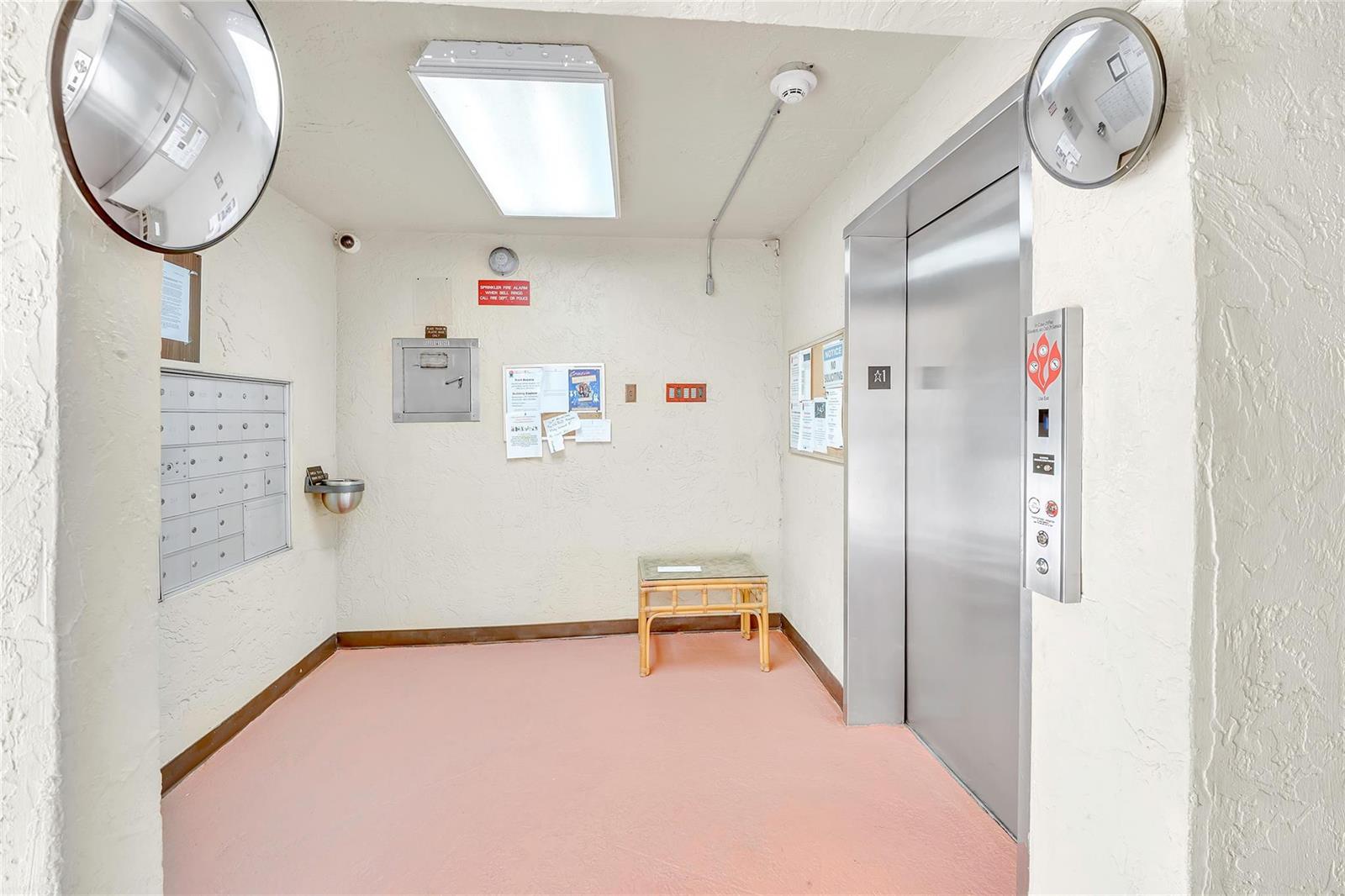 An elevator lobby features a stainless steel elevator, mailboxes, a water fountain, and pink flooring — 4975 E Sabal Palm Boulevard # 408, Tamarac FL 33319, TAMARAC, FL