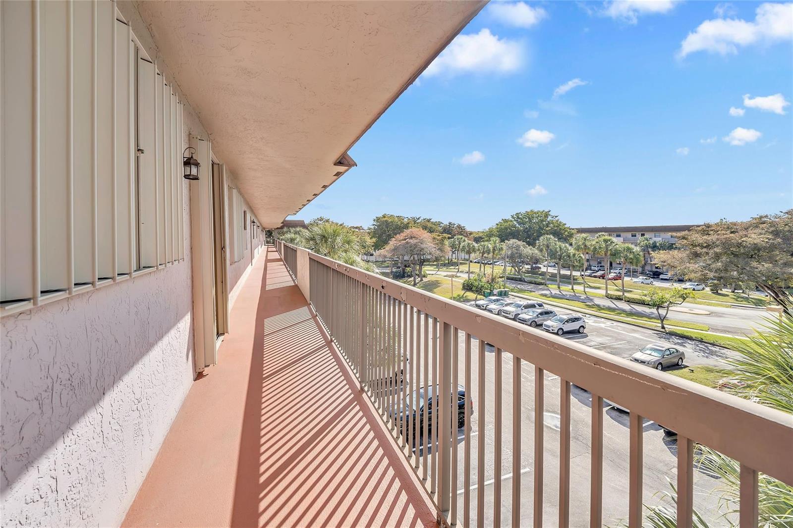 An elevated outdoor walkway with a metal railing overlooks a parking lot and trees — 4975 E Sabal Palm Boulevard # 408, Tamarac FL 33319, TAMARAC, FL