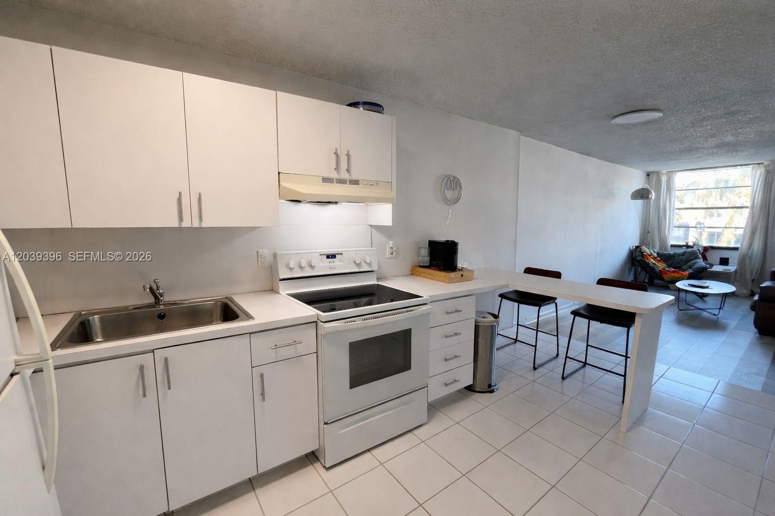 A kitchen features white cabinets, white appliances, a breakfast bar, and light-colored tile flooring — 710 Washington Ave # 319, Miami Beach FL 33139, MIAMI BEACH, FL