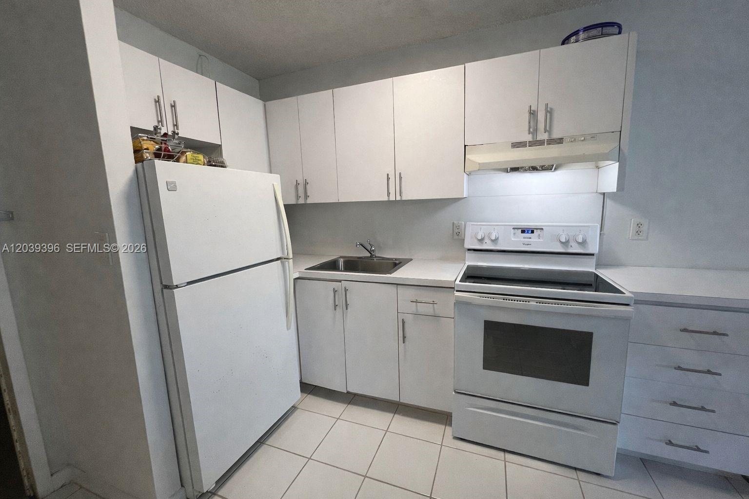 A small kitchen features white cabinets, white appliances, a stainless steel sink, and tiled floors — 710 Washington Ave # 319, Miami Beach FL 33139, MIAMI BEACH, FL