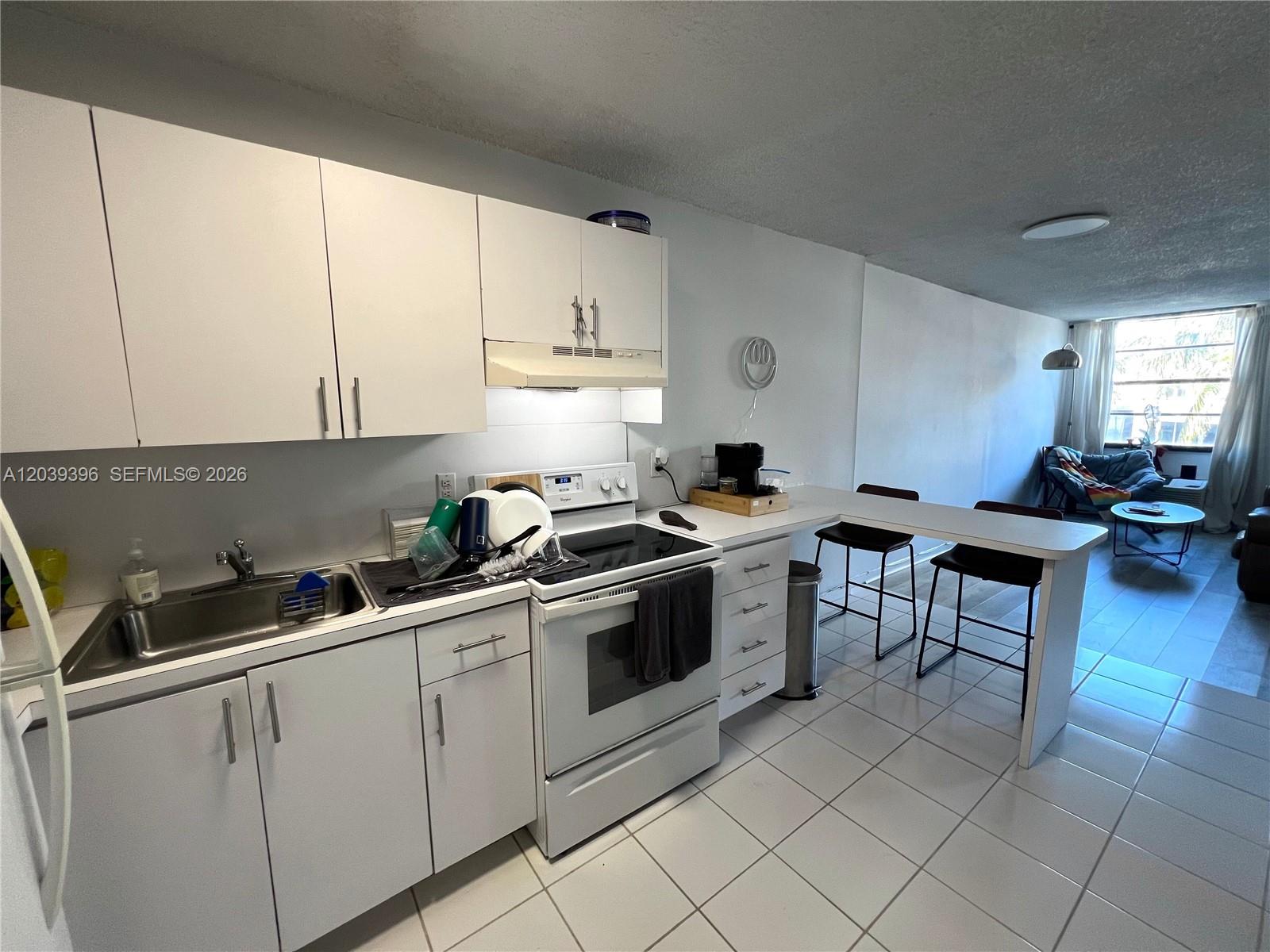 A white kitchen features a breakfast bar, tile flooring, and stainless steel sink — 710 Washington Ave # 319, Miami Beach FL 33139, MIAMI BEACH, FL