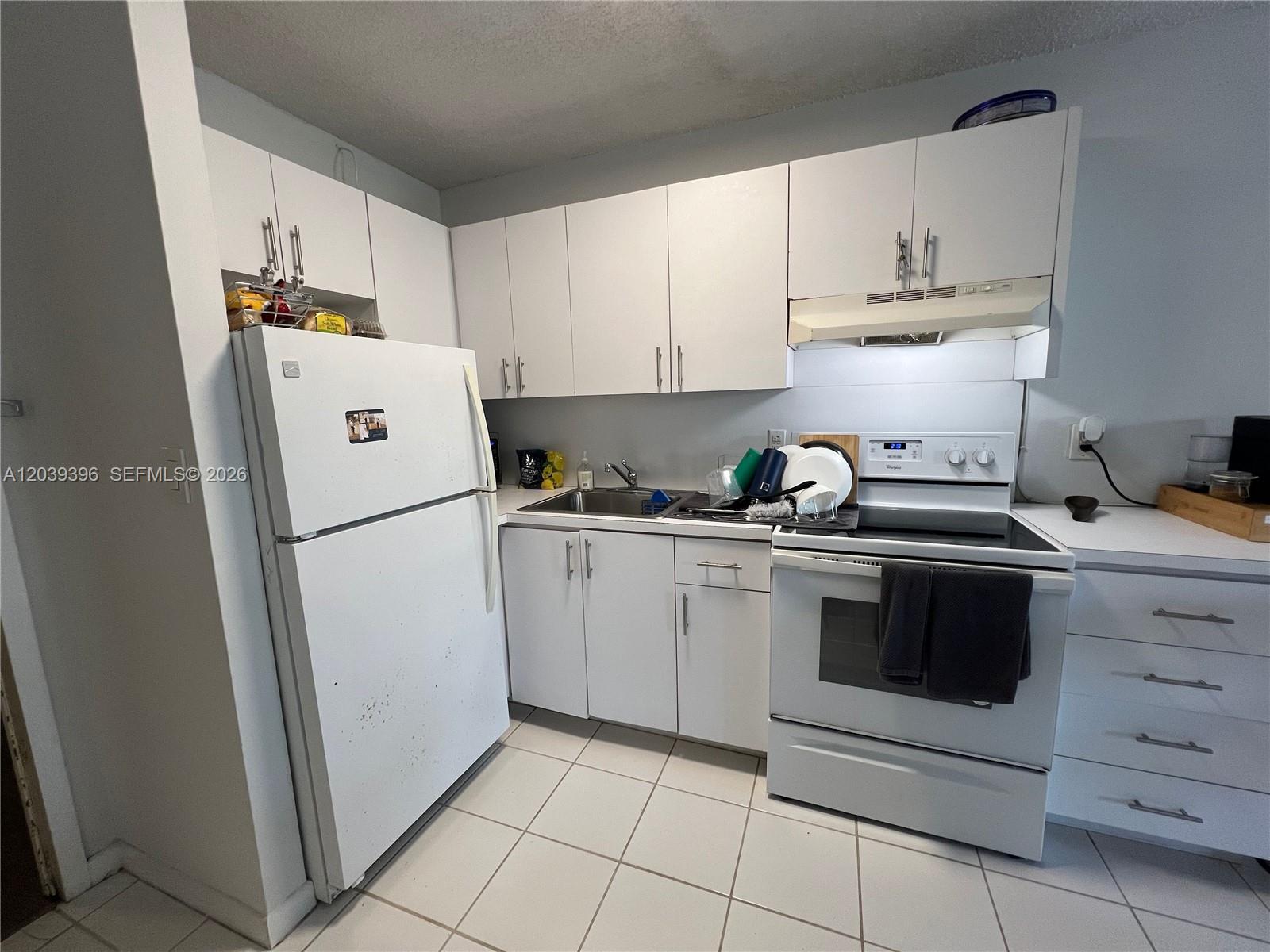A small kitchen features white cabinets, white appliances, and light-colored tiled flooring — 710 Washington Ave # 319, Miami Beach FL 33139, MIAMI BEACH, FL