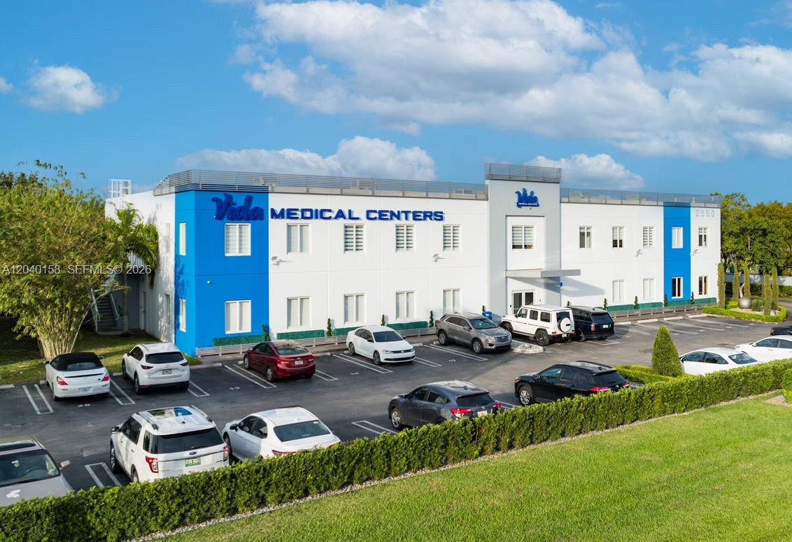 An exterior view of a two-story medical center building with a parking lot in front — 2550 NW 100th Ave, Doral FL 33172, DORAL, FL
