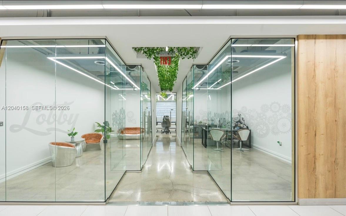 A modern office lobby features glass-walled rooms, polished concrete floors, and a hanging plant installation — 2550 NW 100th Ave, Doral FL 33172, DORAL, FL