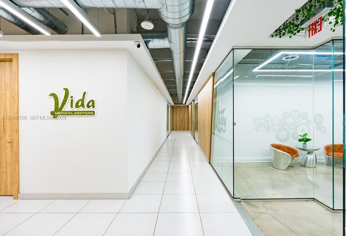 A modern medical office hallway features white tile flooring, glass-walled rooms, and exposed ceiling ductwork — 2550 NW 100th Ave, Doral FL 33172, DORAL, FL