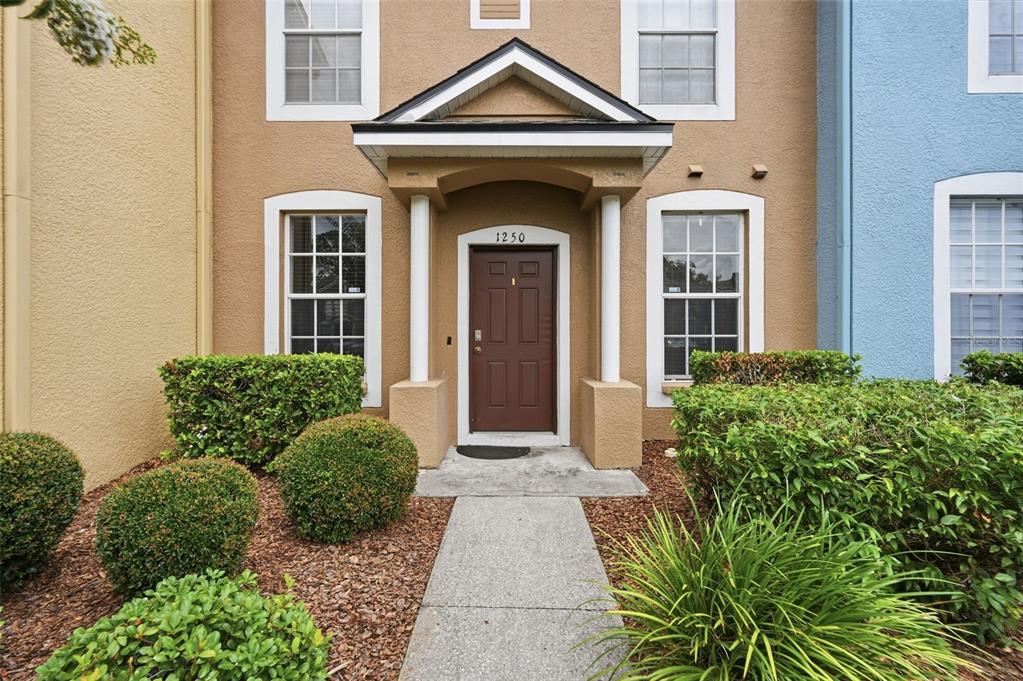 The exterior of a tan townhouse features a brown front door under a small portico — 1250 CHARLESWORTH DRIVE, WESLEY CHAPEL, FL