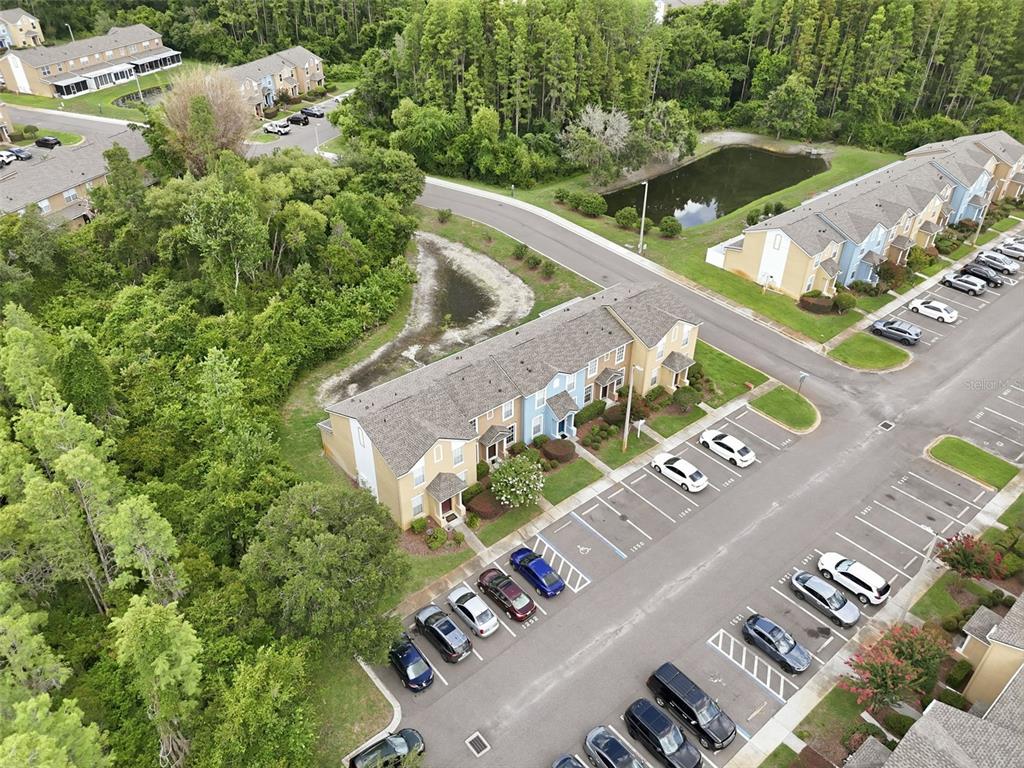 An aerial view shows a multi-unit townhouse building with an adjacent parking lot and pond — 1250 CHARLESWORTH DRIVE, WESLEY CHAPEL, FL