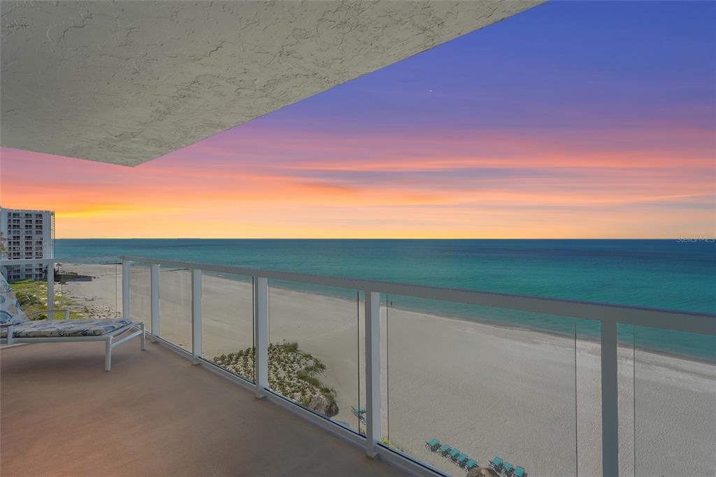 A balcony with a glass railing overlooks a sandy beach and the ocean at sunset — 2425 GULF OF MEXICO DRIVE UNIT 8C, LONGBOAT KEY, FL