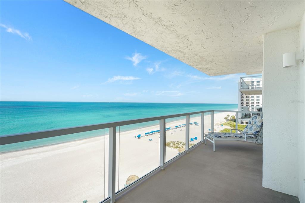 A balcony with a glass railing overlooks a sandy beach and the ocean — 2425 GULF OF MEXICO DRIVE UNIT 8C, LONGBOAT KEY, FL