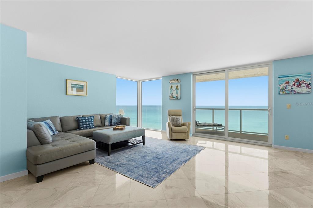 A living room with a gray sectional, blue rug, and floor-to-ceiling windows overlooking the ocean — 2425 GULF OF MEXICO DRIVE UNIT 8C, LONGBOAT KEY, FL