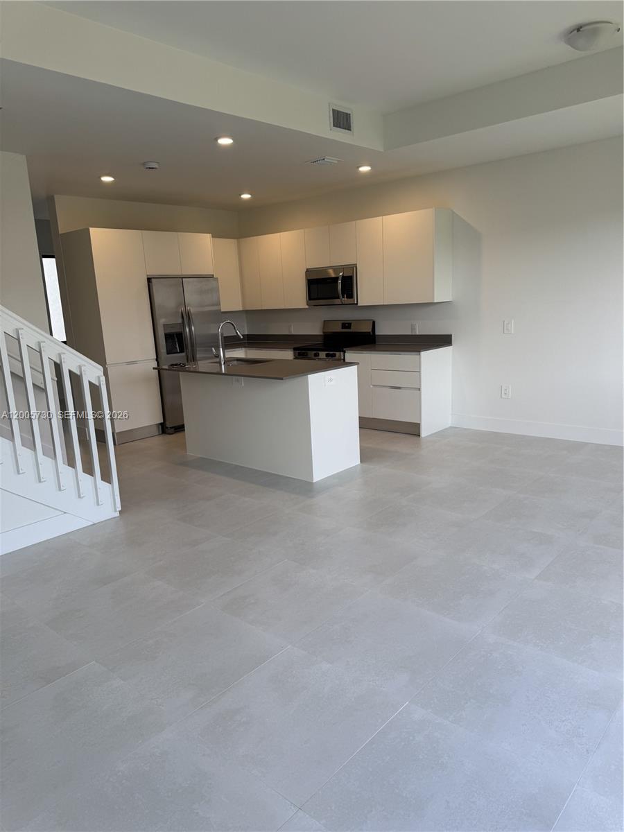 A modern kitchen features white cabinets, stainless steel appliances, a center island, and tiled floors — 18965 SW 344th Ter, Homestead FL 33034, HOMESTEAD, FL