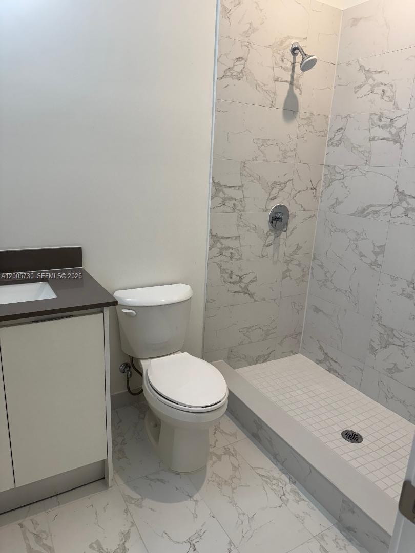 A bathroom features a white vanity, a toilet, and a walk-in shower with marble-patterned tiles — 18965 SW 344th Ter, Homestead FL 33034, HOMESTEAD, FL