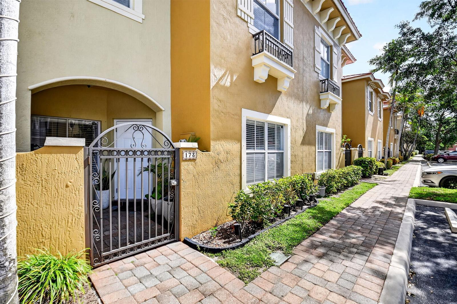 A tan townhouse exterior features a gated courtyard entrance, a brick walkway, and small balconies — 173 Lake Monterey Circle, Boynton Beach FL 33426, BOYNTON BEACH, FL