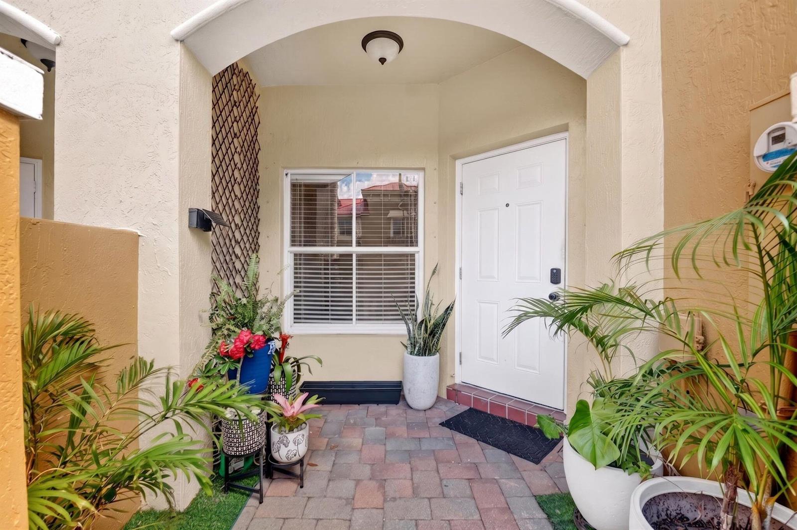 A paved entryway features a white front door, a window with blinds, and several potted plants — 173 Lake Monterey Circle, Boynton Beach FL 33426, BOYNTON BEACH, FL